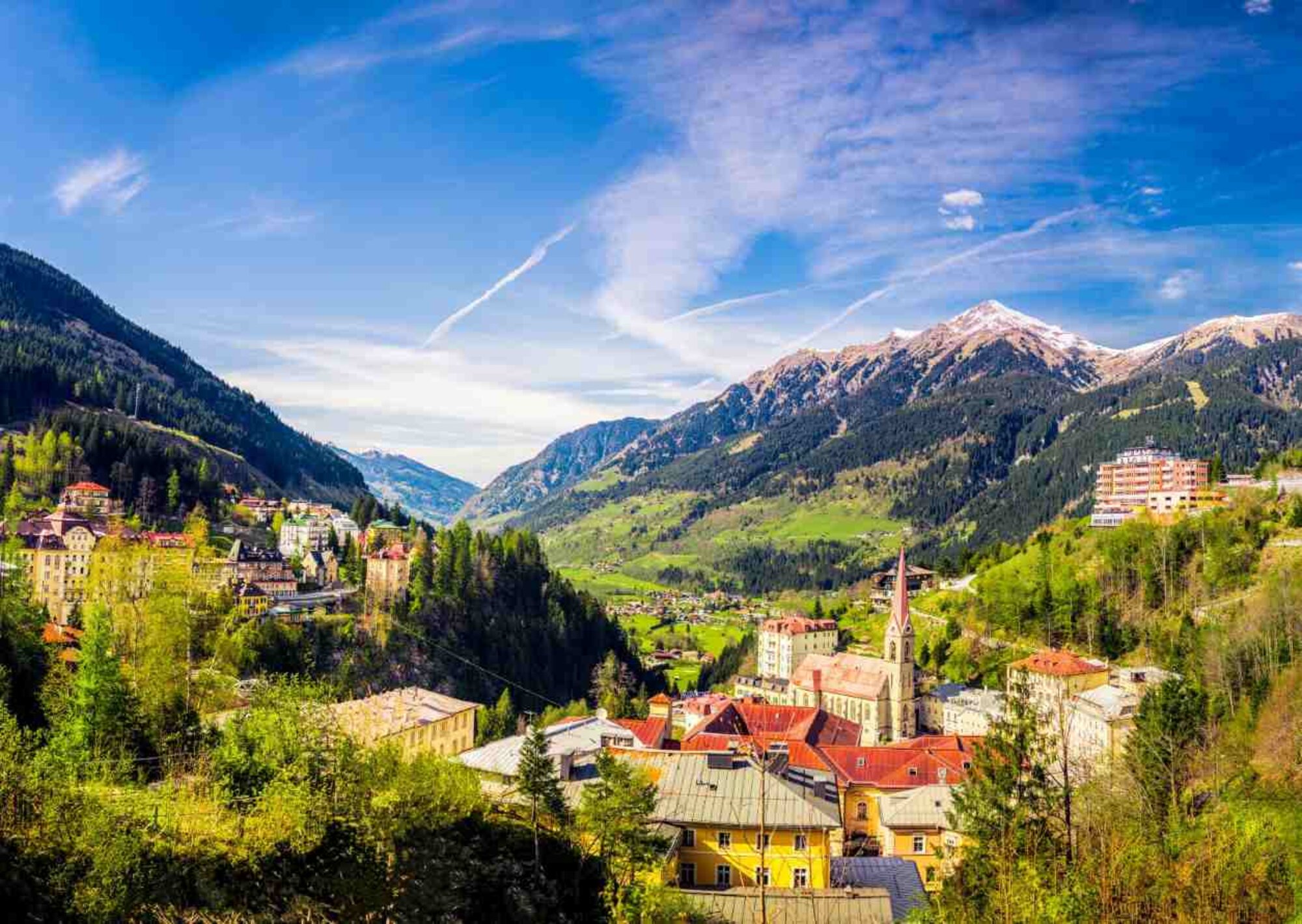 Bad Gastein im Sommer. Man erkennt die Stadt in der Mitte und im Hintergrund liegen grüne Berge und Gipfel.