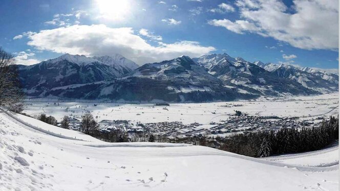 Panoramaaufnahme vom eingeschneiten Piesendorf. Man sieht den Ort von einem Berg aus. Die Sonne scheint und der Himmel ist nur leicht bewölkt