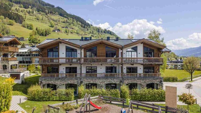 Das Appartement Haus Mitterwirt in sommerlicher Atmosphäre. Man sieht das Gebäude aus der Frontansicht und im Hintergrund sind grüne Hügel