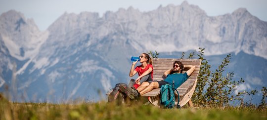 Wanderer auf einer Bank vor Alpenkulisse